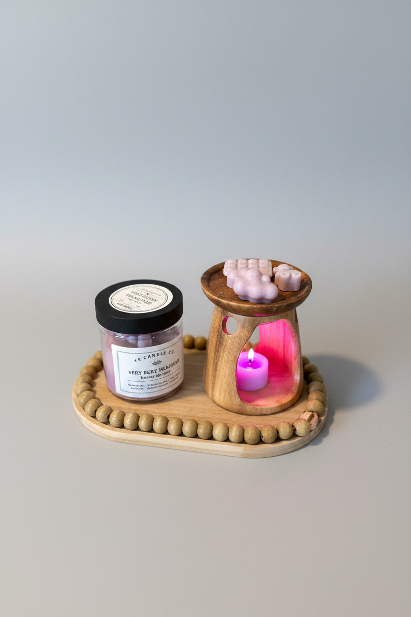 A wax melt in the shape of a milkshake with cream and cherry on top, next to a jar with a label, on a wooden tray.