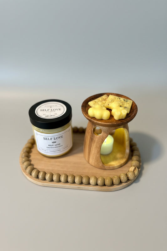 A wooden wick holder with two jars of wax tarts on top, one labeled 'Patchouli' and the other labeled 'Santalwood'. The wax tarts are in the process of melting.