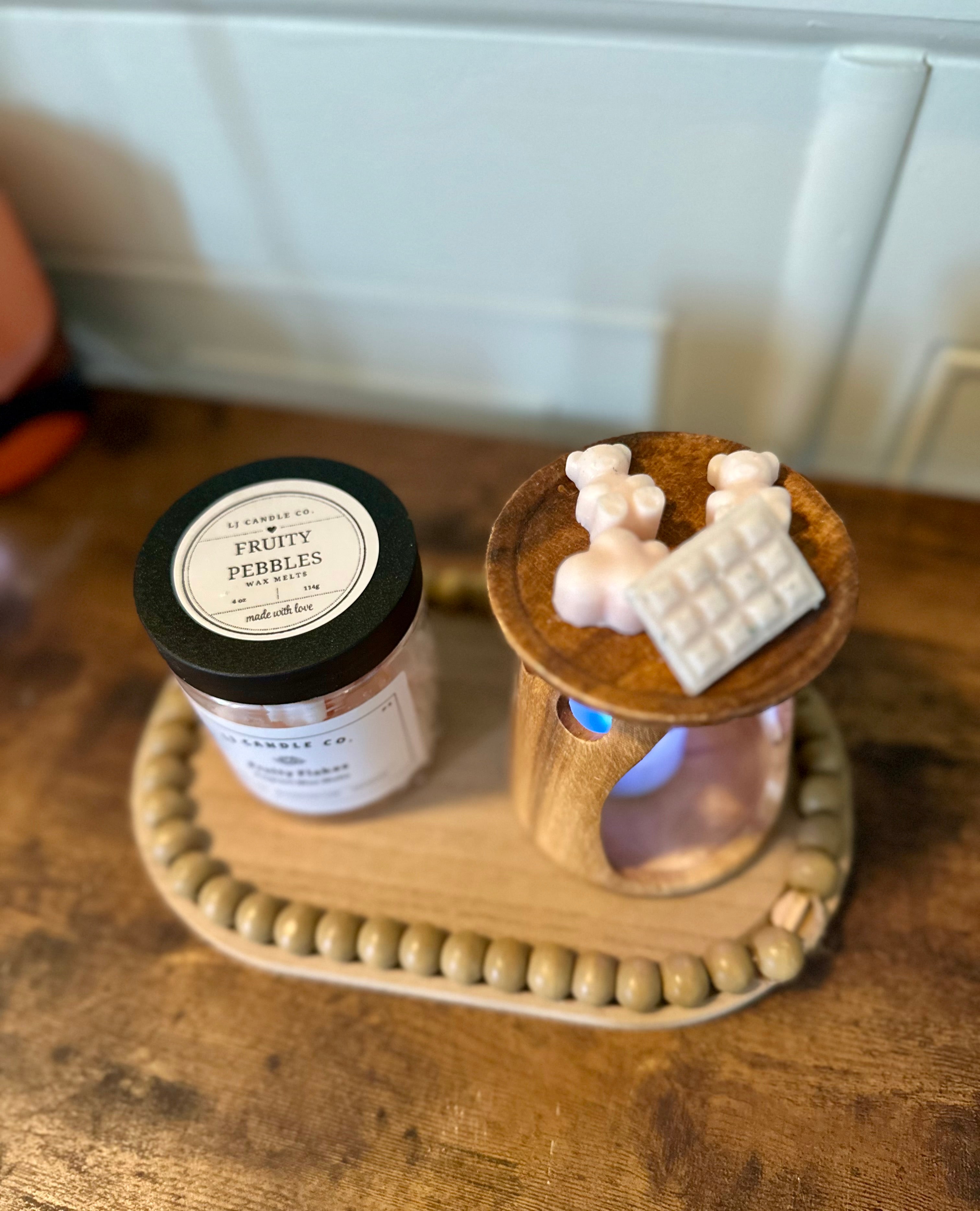 A wax melt container labeled 'Fruity Flakes' with a cereal-shaped wax melt on top, placed on a wooden surface.